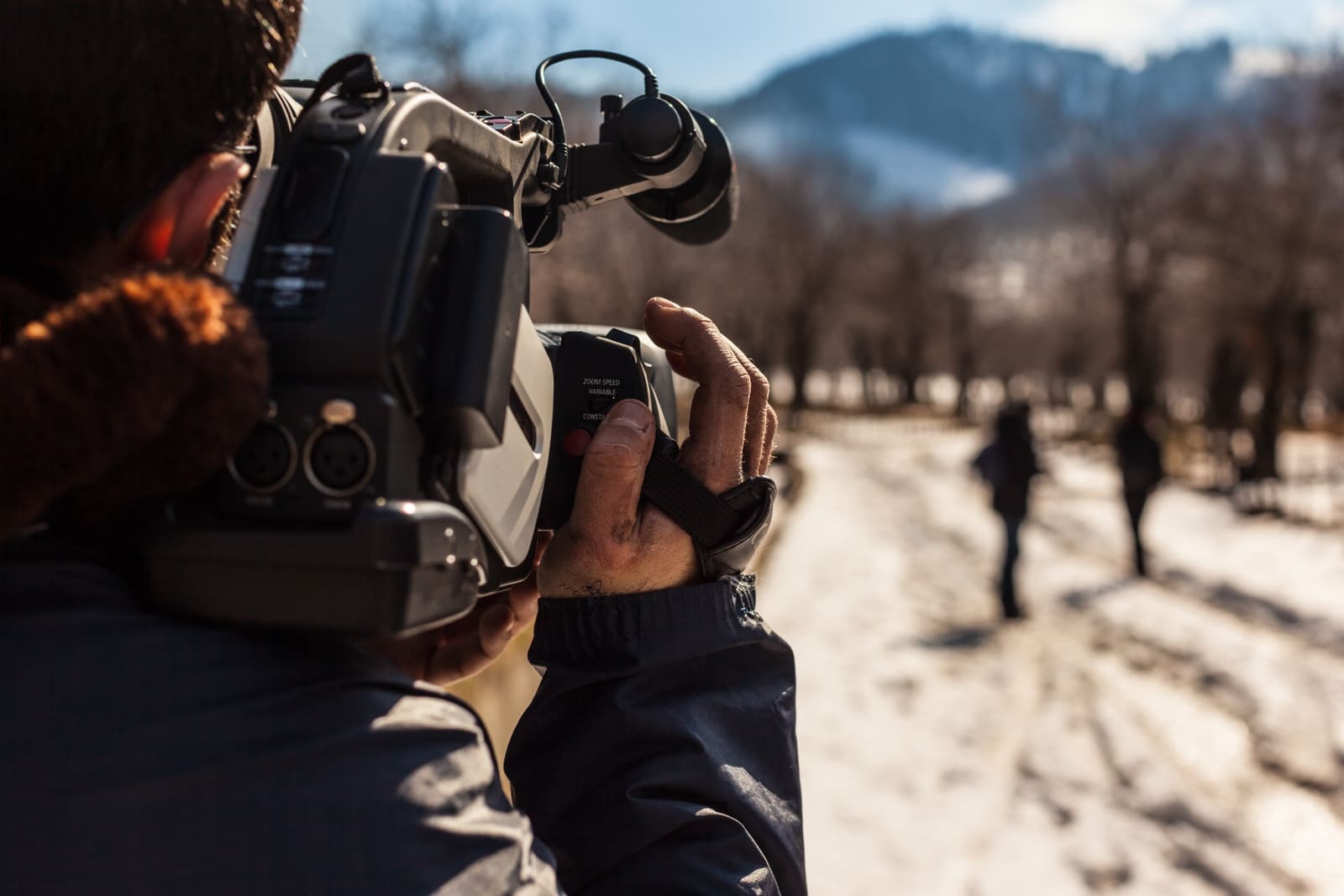 A sole cameraman shooting outdoors in rugged landscape with snow covered hills making a documentary film in the UK