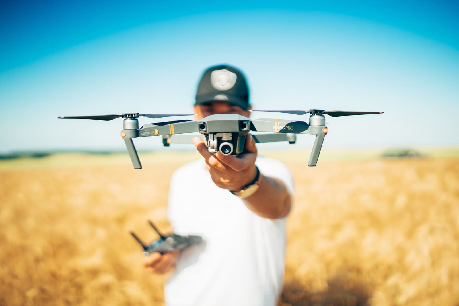 Demonstrating Modern Filmmaking Techniques by a cinematographer holding a drone whilst standing in a large field of barley with a stunning clear blue sky in the background