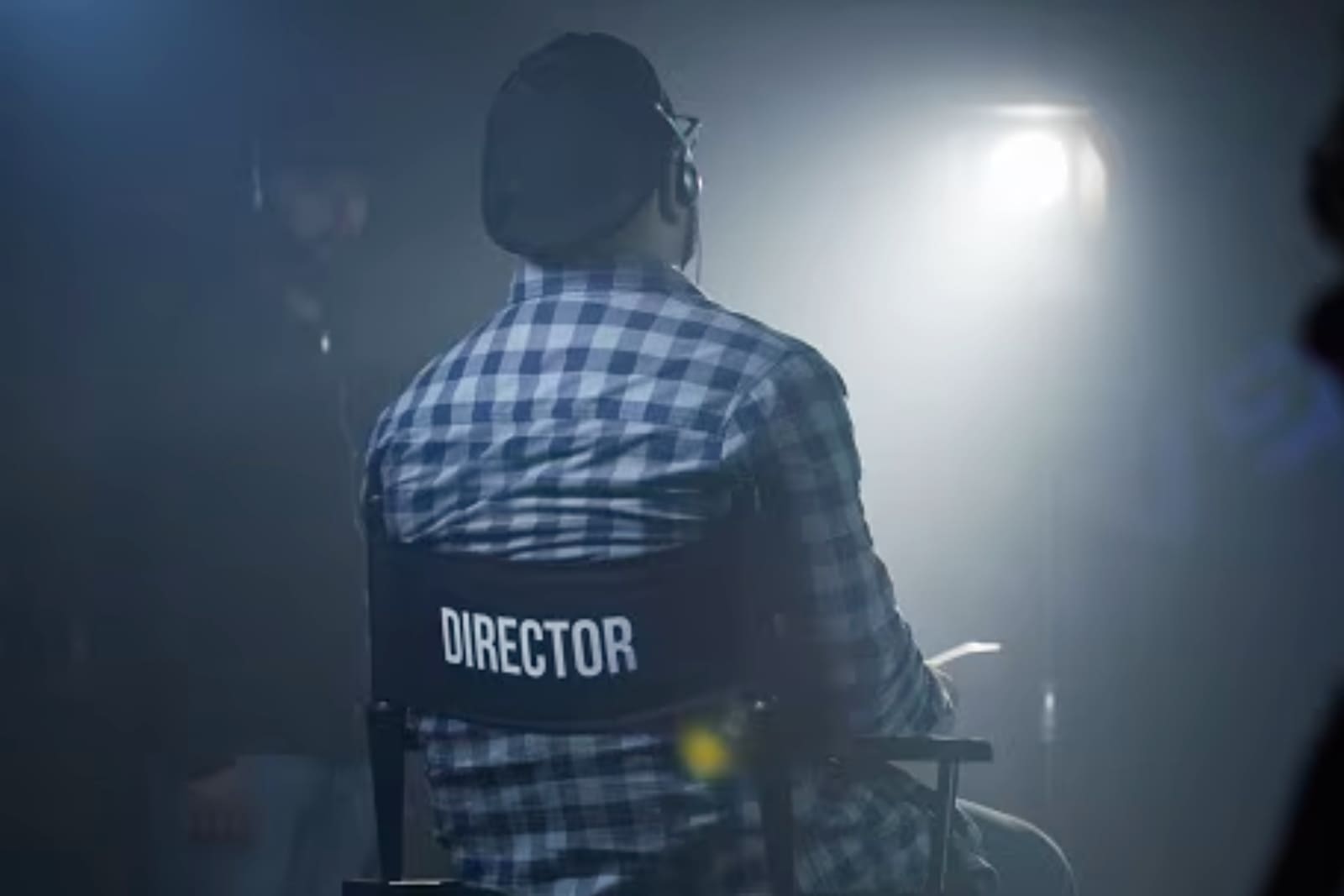 A male director sat in a director's chair facing away from the camera. The word director is written on the back of the chair. Directing Dynamics.