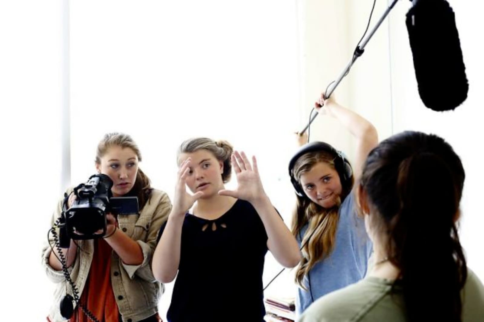 A group of female filmmakers holding cameras, boom mics, and creating a frame with their hands demonstrating student filmmaking in the UK